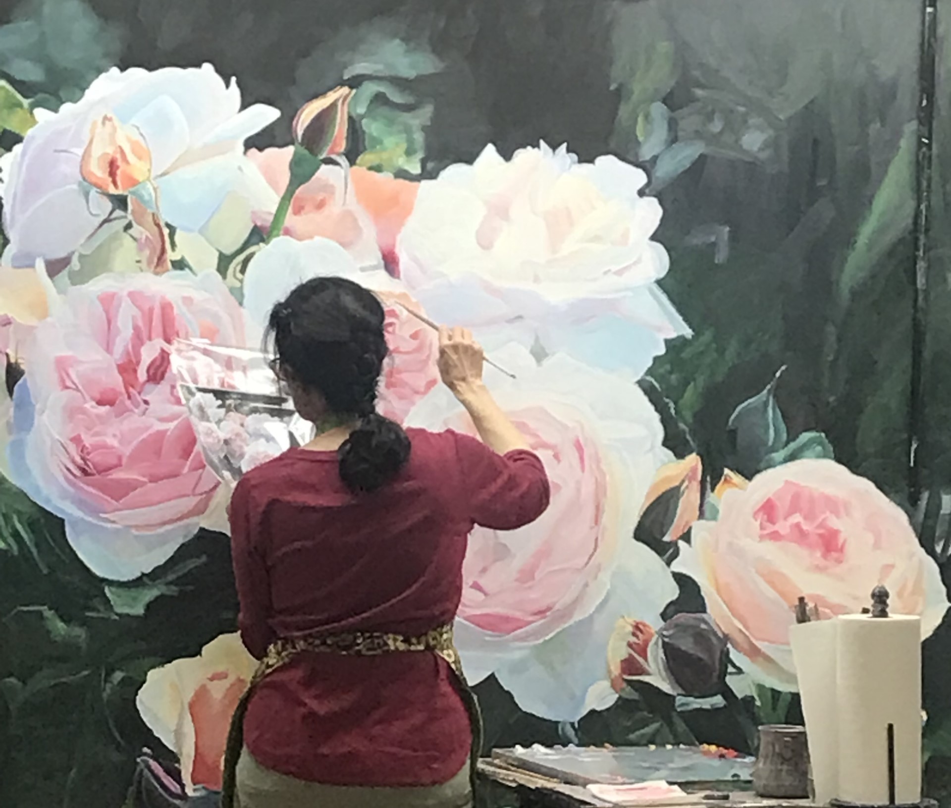 A back view of a woman with dark hair in front of large painting of flowers.